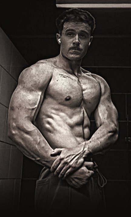 Janco van der Walt, shirtless, arms folded in front of him in a dark gym bathroom