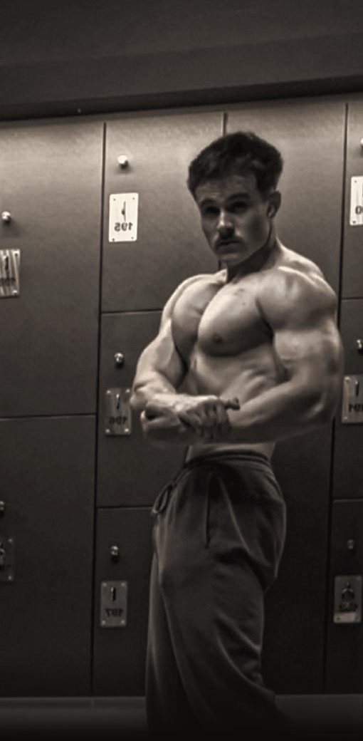 Janco van der Walt doing a side chest pose in a gym locker room